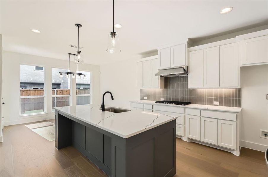 Kitchen with hanging light fixtures, a kitchen island with sink, exhaust hood, white cabinetry, and light hardwood / wood-style flooring