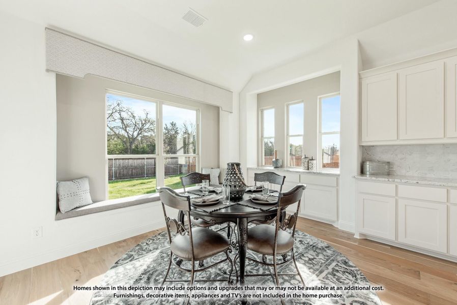 Bright breakfast nook with round dining table, window seat, and hardwood floors next to white kitchen cabinets