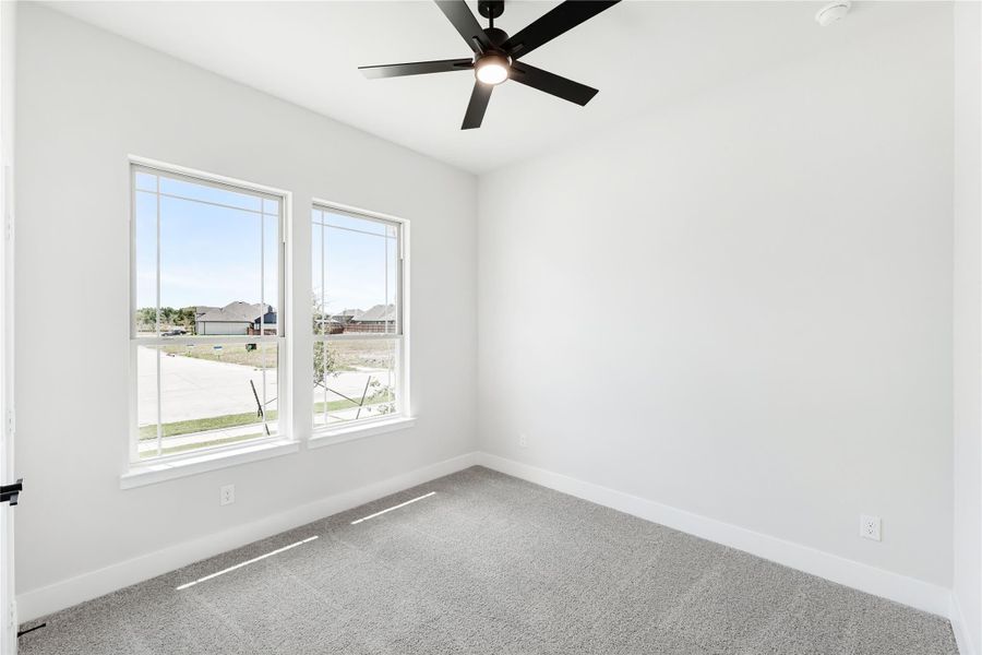 Empty bedroom with gray carpet, black ceiling fan, and two windows with neighborhood view