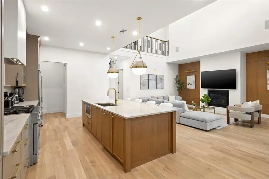 Open-concept living space featuring light wood-finish flooring, a kitchen island with stone countertop, and a fireplace with a mounted television