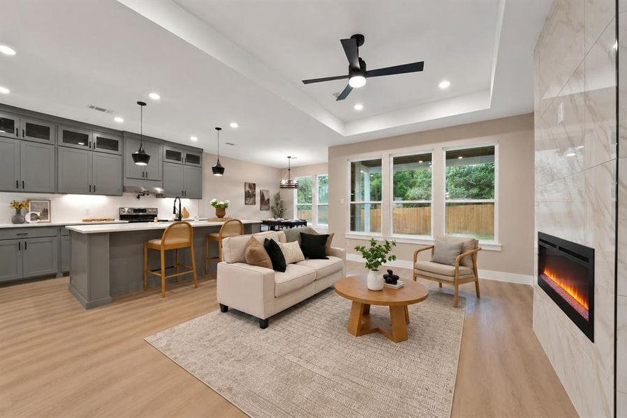 Open-concept living space featuring wood-finish flooring, a contemporary fireplace with a tiled surround, and a tray ceiling with recessed lighting Open-concept living space featuring wood-finish flooring, a contemporary fireplace with a tiled surround, and a tray ceiling with recessed lighting