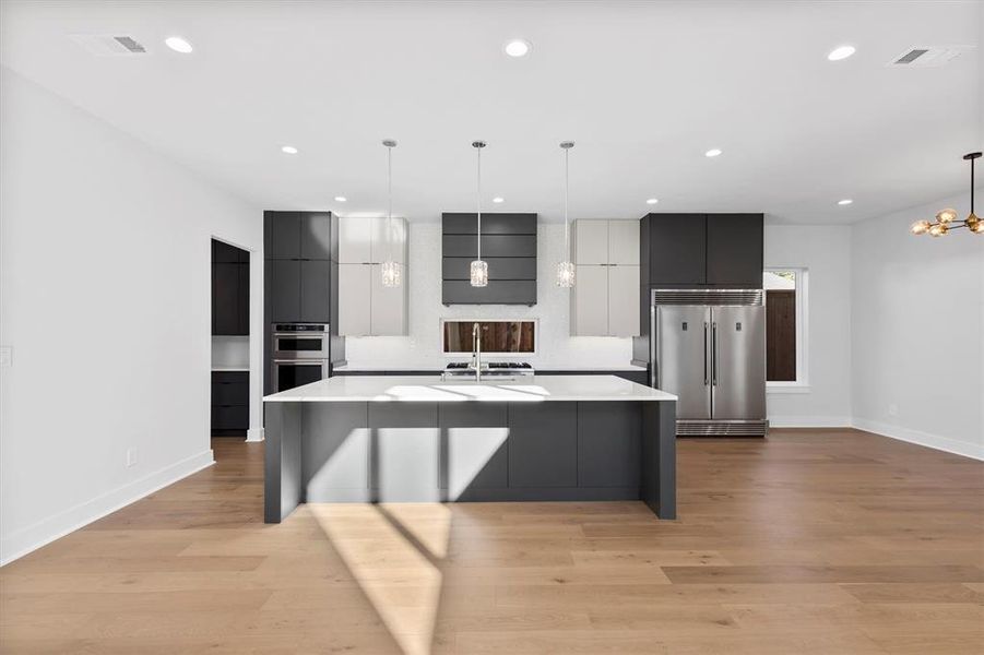 Kitchen with appliances with stainless steel finishes, extractor fan, a large island with sink, decorative light fixtures, and light hardwood / wood-style floors