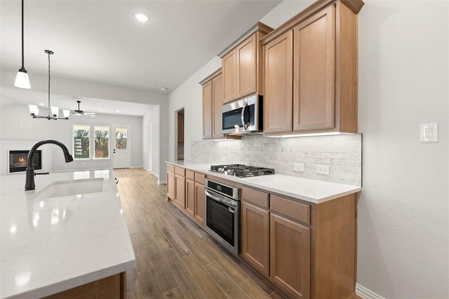 Kitchen with decorative light fixtures, a glass covered fireplace, stainless steel appliances, light stone countertops, and backsplash Kitchen with decorative light fixtures, a glass covered fireplace, stainless steel appliances, light stone countertops, and backsplash