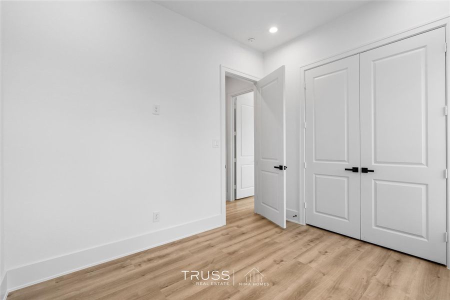 This thoughtfully designed bedroom balances simplicity and warmth with warm toned floors, soft recessed lighting, and clean architectural lines. Dual closets offer functional storage while maintaining the home’s calm, modern aesthetic, a versatile space equally suited for guests or everyday living.