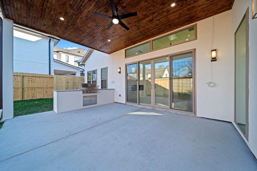 This inviting outdoor space features a fully equipped kitchen with a built-in grill and sink, perfect for hosting BBQs and gatherings. The covered patio boasts a beautiful wood-paneled ceiling with recessed lighting and a ceiling fan, creating a comfortable area to enjoy year-round. With seamless access to the interior living spaces through sliding glass doors, this outdoor retreat combines functionality and style for the ultimate entertaining experience.