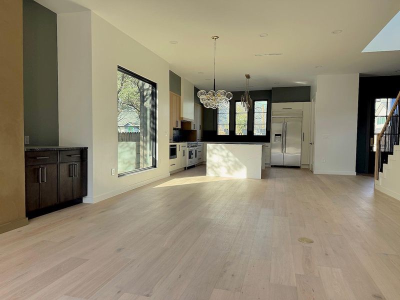 Unfurnished living room featuring a wealth of natural light, a notable chandelier, stairs, and light wood finished floors