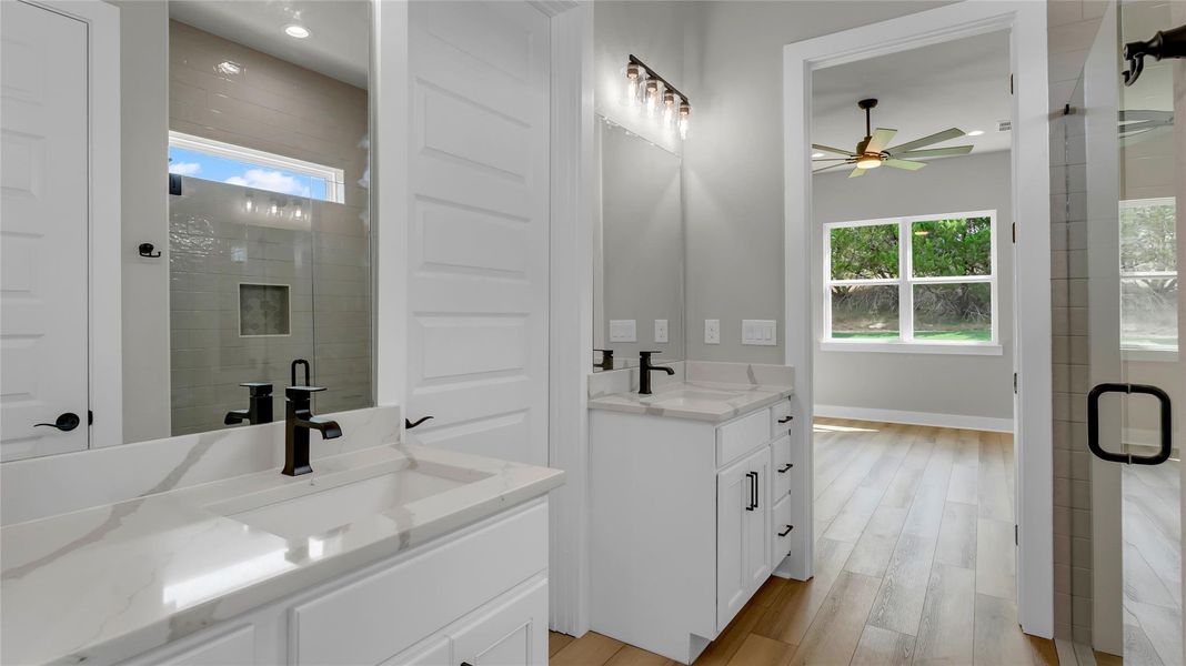 Bathroom with two vanities, light wood-type flooring, a shower stall, and a ceiling fan