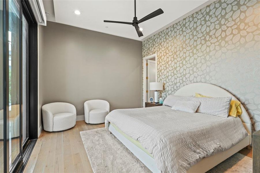 Bedroom with light wood finished floors, ceiling fan, recessed lighting, and wallpapered walls Bedroom with light wood finished floors, ceiling fan, recessed lighting, and wallpapered walls