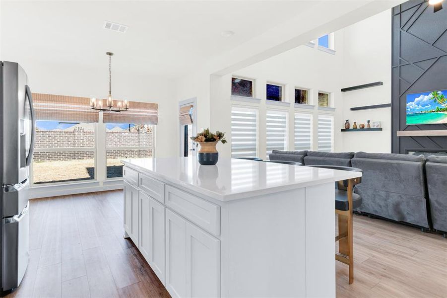 Kitchen featuring a kitchen island, stainless steel fridge with ice dispenser, hanging light fixtures, white cabinets, and light stone counters Kitchen featuring a kitchen island, stainless steel fridge with ice dispenser, hanging light fixtures, white cabinets, and light stone counters