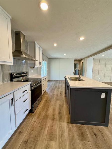 Dual tone kitchen with two tone cabinets, stainless steel range with electric stovetop, decorative backsplash, light countertops, and light wood-style floors Dual tone kitchen with two tone cabinets, stainless steel range with electric stovetop, decorative backsplash, light countertops, and light wood-style floors