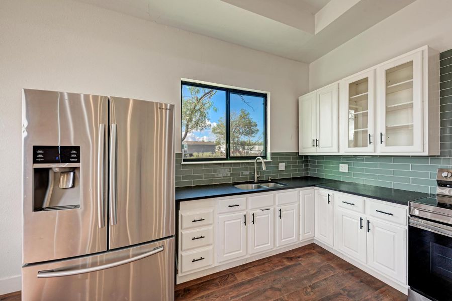 Dark countertops contrast with white cabinetry and a glass tile backsplash under high ceilings.