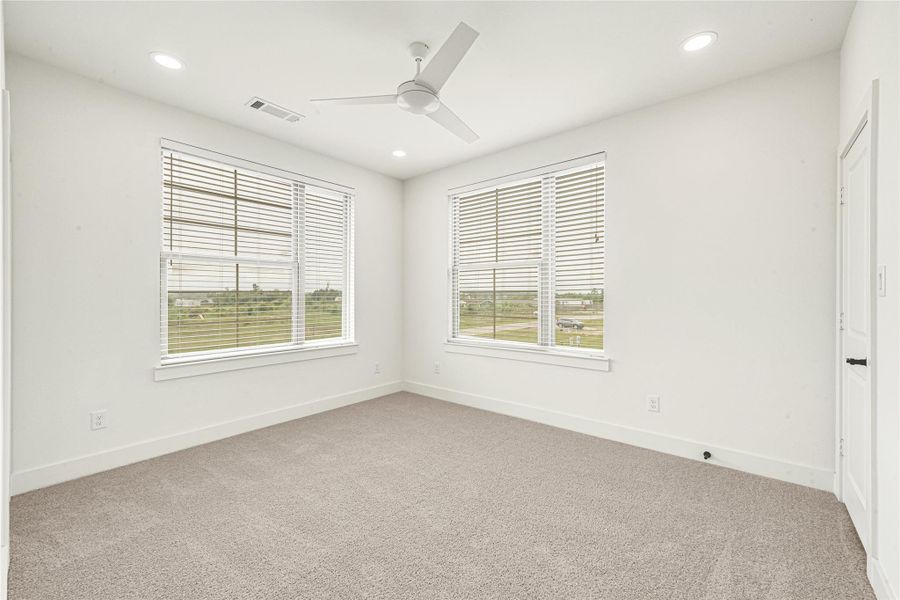 Welcome to Secondary Bedroom 2! This bright and inviting space mirrors the home’s modern aesthetic with soft carpeting, modern lighting, two large windows with a view to the front and side of the home