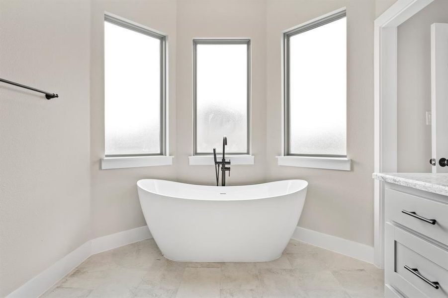 Bathroom with a wealth of natural light, a tub to relax in, and vanity