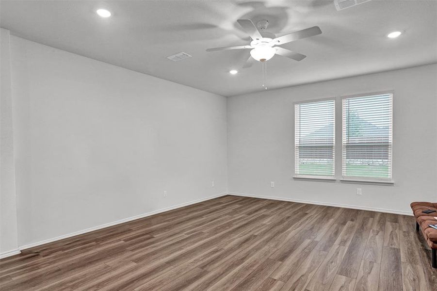 Spacious room featuring wood-finish flooring, white walls, and a ceiling fan with integrated lighting
