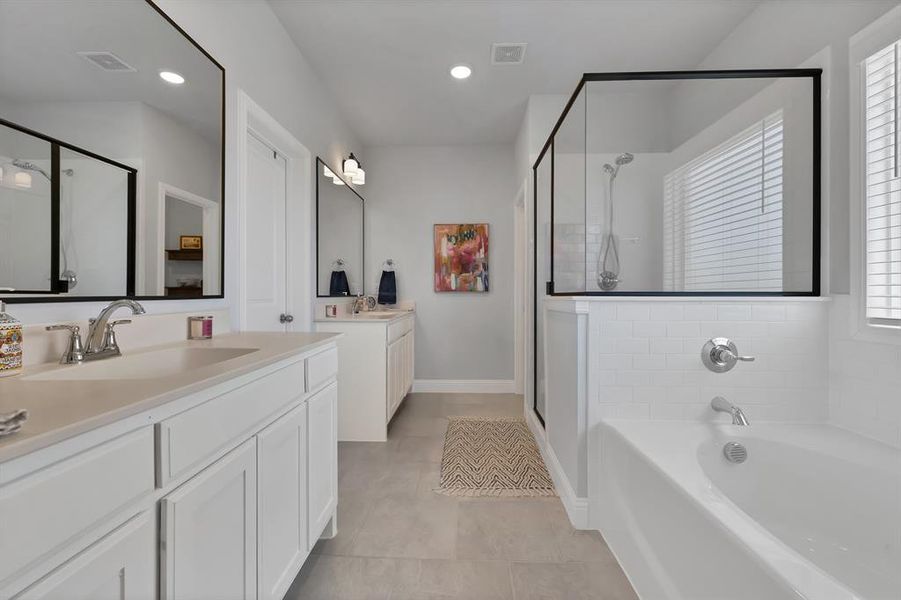 Full bathroom featuring two vanities, a bath, a stall shower, light tile patterned flooring, and plenty of natural light Full bathroom featuring two vanities, a bath, a stall shower, light tile patterned flooring, and plenty of natural light