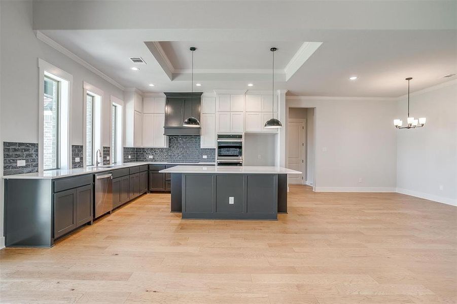 Kitchen featuring a kitchen island, hanging light fixtures, stainless steel appliances, white cabinets, and light hardwood / wood-style flooring