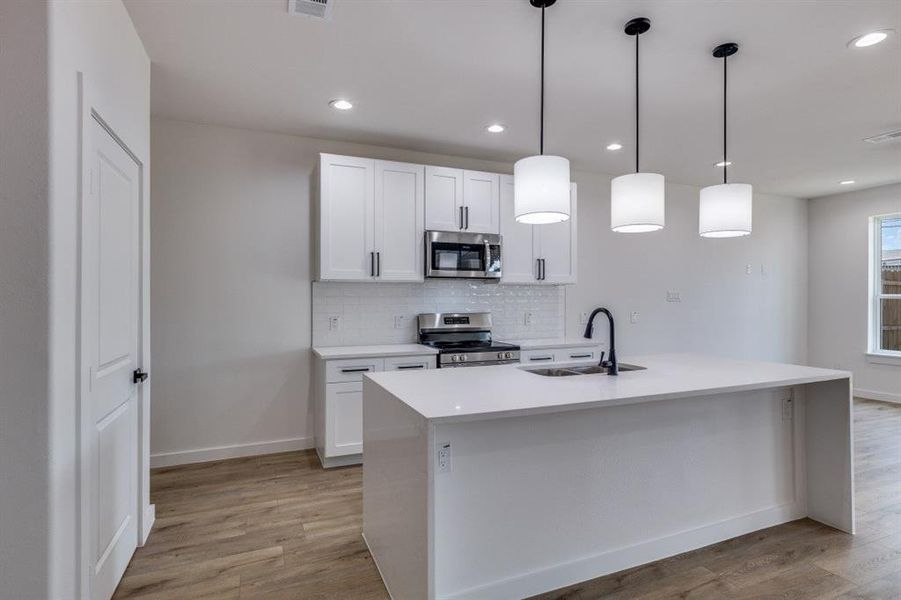 Kitchen with backsplash, pendant lighting, light stone counters, stainless steel appliances, and white cabinets Kitchen with backsplash, pendant lighting, light stone counters, stainless steel appliances, and white cabinets