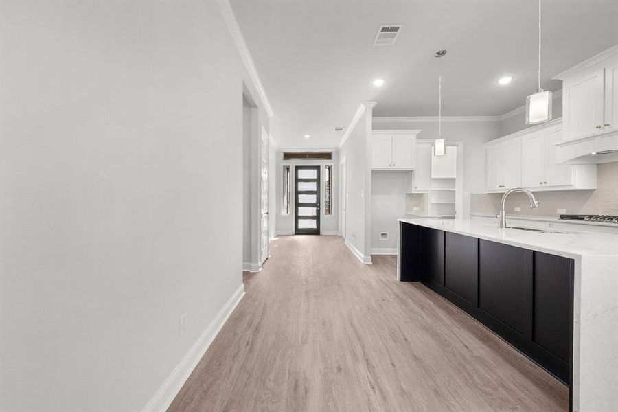 Kitchen with crown molding, white cabinets, light wood-style flooring, decorative light fixtures, and tasteful backsplash