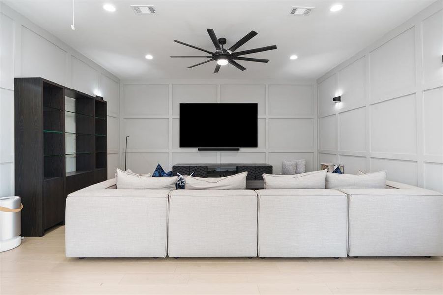 Living area with visible vents, ceiling fan, and a decorative wall