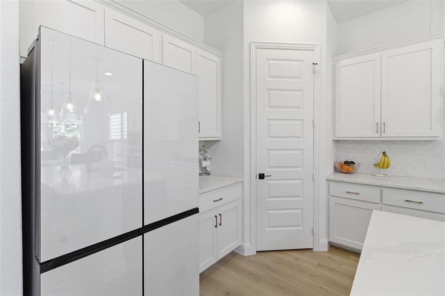 Contemporary kitchen featuring white cabinetry with gold-toned hardware, light wood-finish flooring, and a white paneled door with a black handle