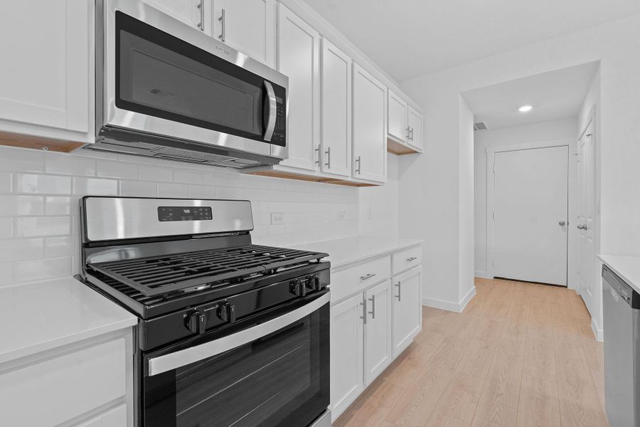 Kitchen with stainless steel appliances, white cabinets, light wood-type flooring, decorative backsplash, and light stone counters