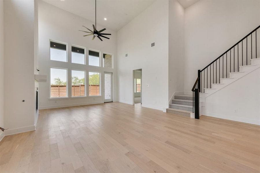 Unfurnished living room with stairway, light wood-type flooring, a high ceiling, ceiling fan, and recessed lighting Unfurnished living room with stairway, light wood-type flooring, a high ceiling, ceiling fan, and recessed lighting