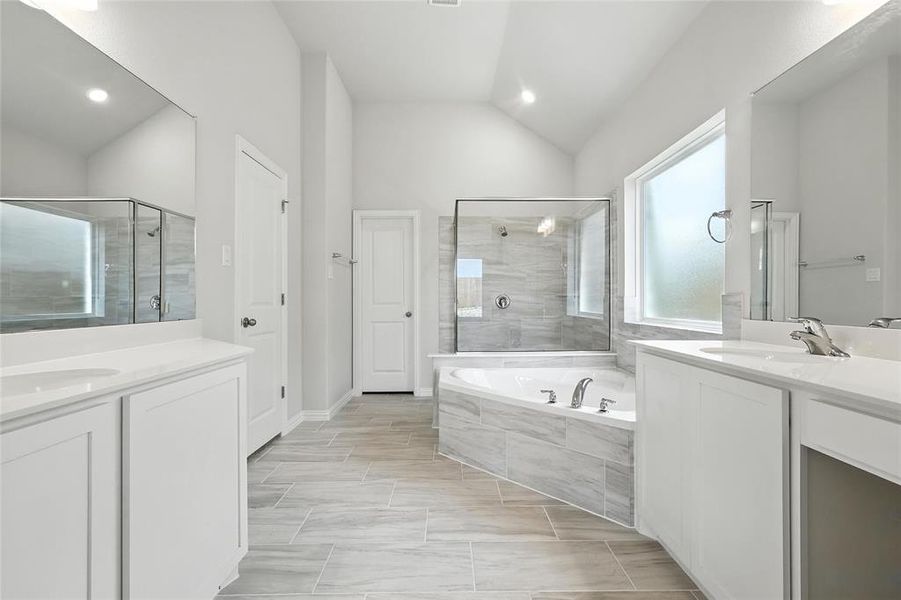 Full bath featuring two vanities, a stall shower, a bath, vaulted ceiling, and recessed lighting