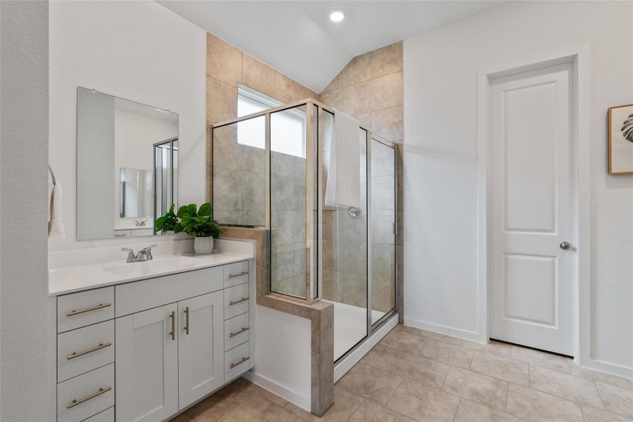 A spacious bathroom featuring a modern vanity, a glass-enclosed shower, and sleek tile flooring.