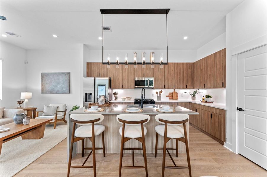 Striking and modern kitchen island serves as the centerpiece of this open-concept culinary space, featuring a waterfall quartz countertop that flows seamlessly down one side for a sculptural, high-end look. The island is framed by minimalist cabinetry in matte finishes, paired with bold pendant lighting that adds a touch of sophistication. Integrated bar seating invites casual dining and conversation, while the clean lines and neutral palette enhance the island’s sleek aesthetic.