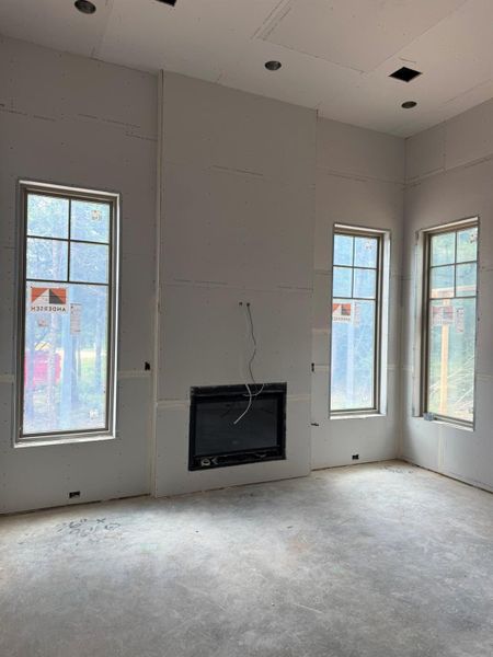 A living space ready for finishes features a central fireplace and ample natural illumination through tall windows.