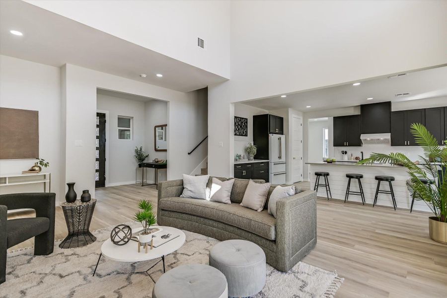 An airy living space with soaring ceilings and light wood flooring, openly flowing into a contemporary kitchen.