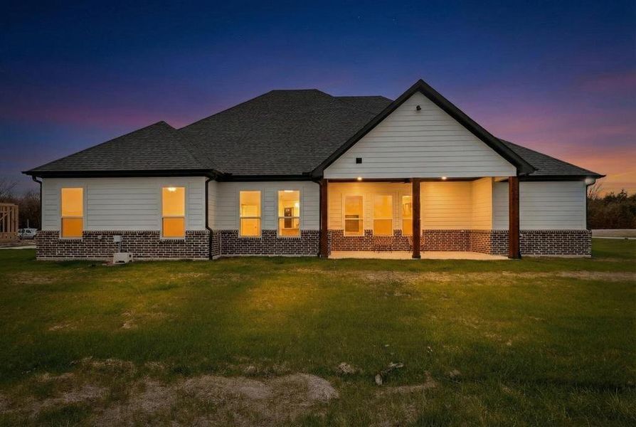 Back of house at dusk with a lawn, a patio area, brick siding, and roof with shingles Back of house at dusk with a lawn, a patio area, brick siding, and roof with shingles