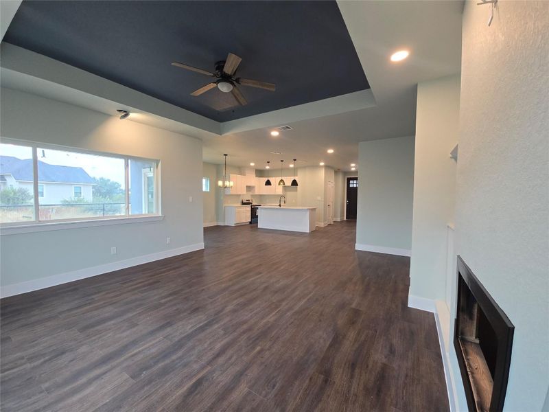 Unfurnished living room featuring a raised ceiling, recessed lighting, a ceiling fan, dark wood-style flooring, and a chandelier