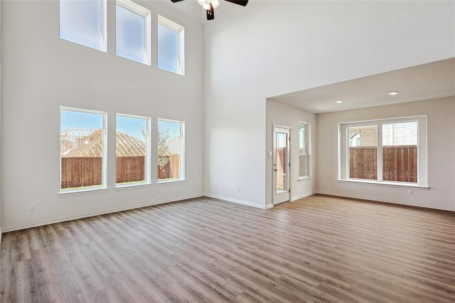 Unfurnished living room with ceiling fan, light wood-type flooring, and a high ceiling