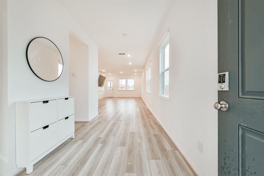 Bright, modern entryway with wood flooring. Open layout leads to a spacious living area with natural light from multiple windows.