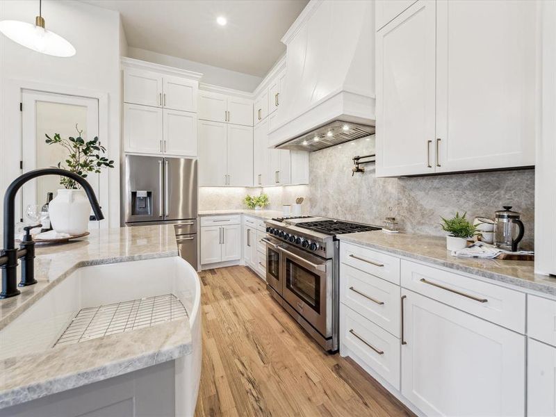 Kitchen featuring light hardwood / wood-style flooring, premium range hood, decorative light fixtures, white cabinets, and appliances with stainless steel finishes