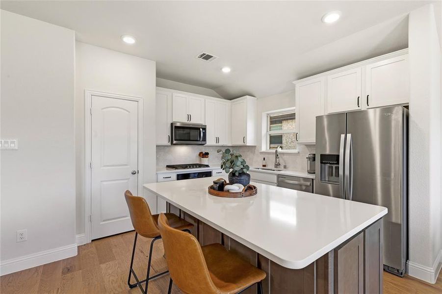 Modern kitchen featuring a large island with a light-toned countertop, white cabinetry, stainless steel appliances, wood-finish flooring, and recessed lighting