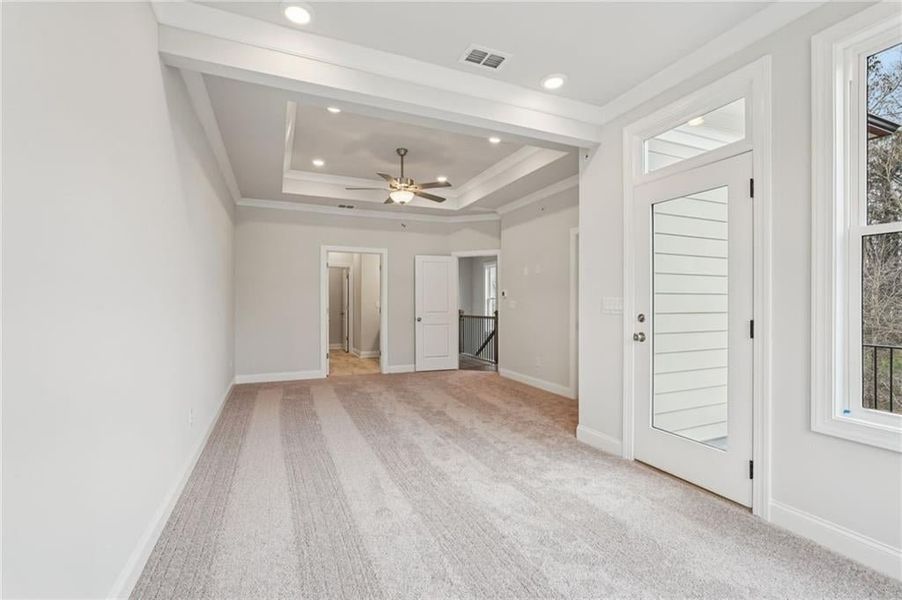 Empty room featuring light carpet, a raised ceiling, a ceiling fan, ornamental molding, and recessed lighting