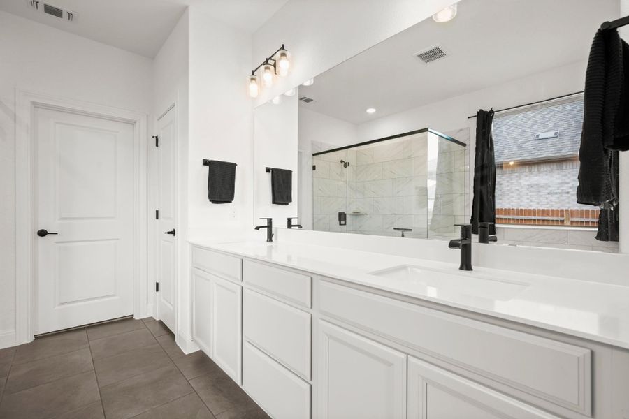 Full bath featuring a shower stall, dark tile patterned flooring, and double vanity Full bath featuring a shower stall, dark tile patterned flooring, and double vanity