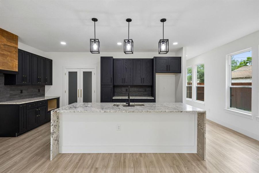 Kitchen island featuring a waterfall countertop, accented by three pendant lights Kitchen island featuring a waterfall countertop, accented by three pendant lights