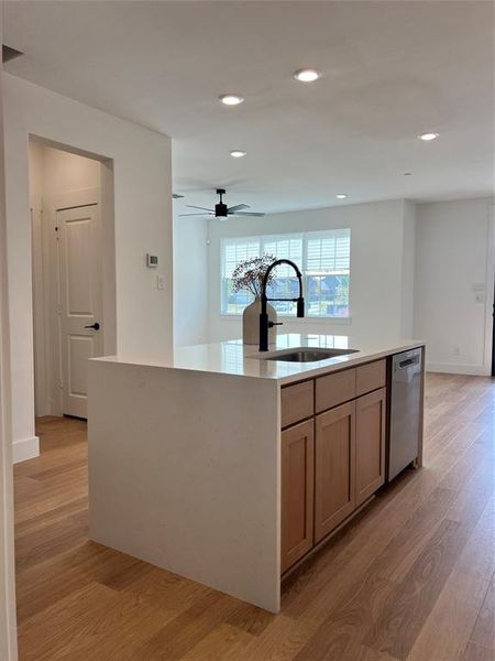 Kitchen with light wood-style floors, light stone counters, recessed lighting, a kitchen island with sink, and dishwashing machine