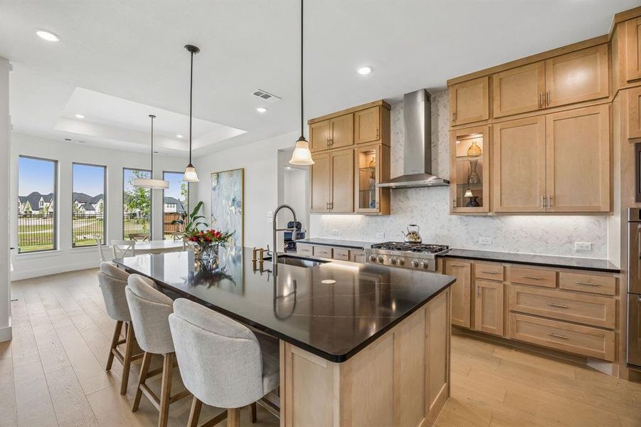 Kitchen with a breakfast bar area, light wood finished floors, backsplash, a kitchen island with sink, and a tray ceiling