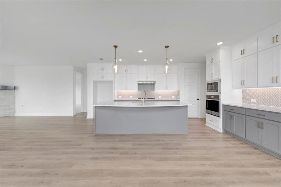 Bright kitchen featuring an expansive central island with a contrasting gray base, white upper cabinetry, and integrated stainless steel appliances