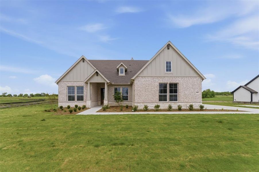 View of front of house featuring board and batten siding, brick siding, and a front lawn