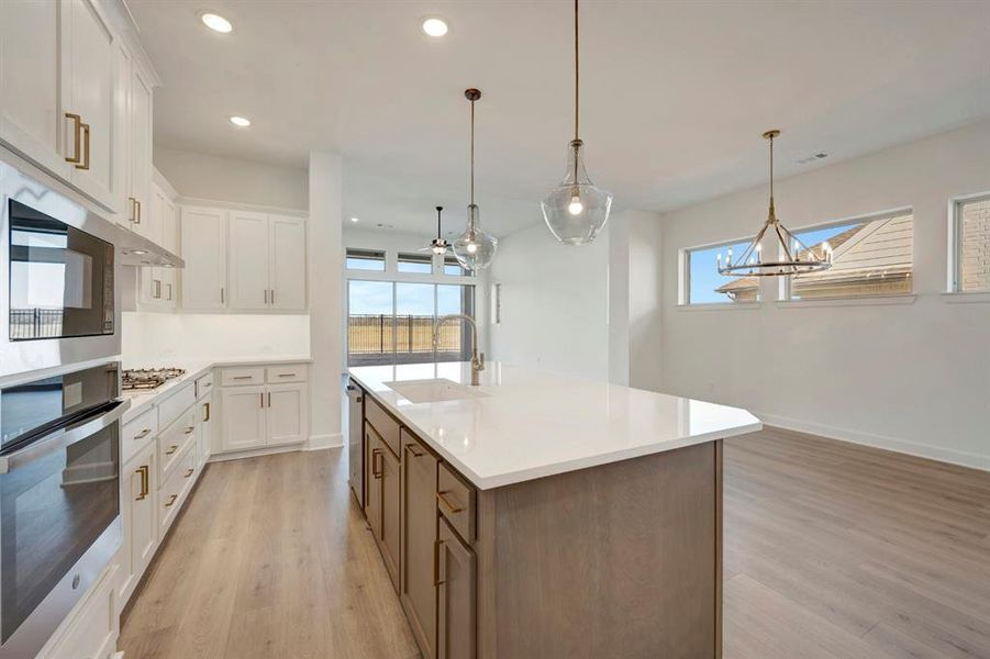 Dual tone kitchen featuring two tone color scheme, stainless steel appliances, pendant lighting, a center island with sink, and light wood-style flooring Dual tone kitchen featuring two tone color scheme, stainless steel appliances, pendant lighting, a center island with sink, and light wood-style flooring