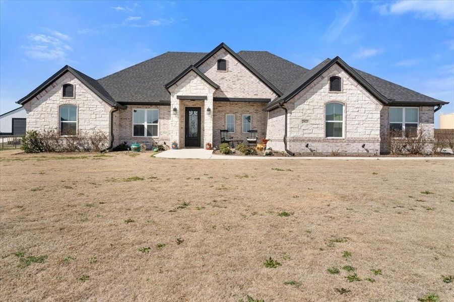 French country style house featuring a shingled roof, a front lawn, and brick siding