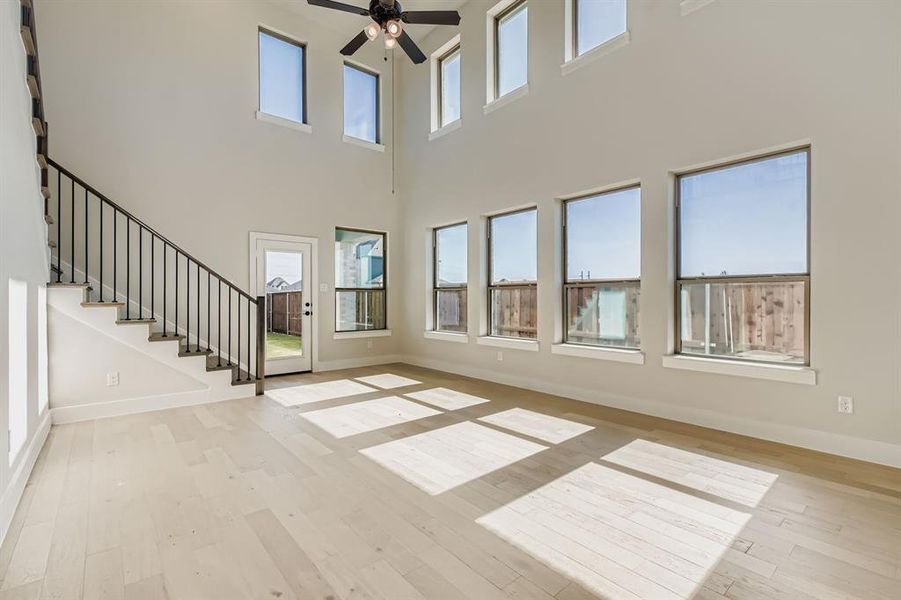 Unfurnished living room featuring a ceiling fan, hardwood / wood-style flooring, stairway, and a towering ceiling