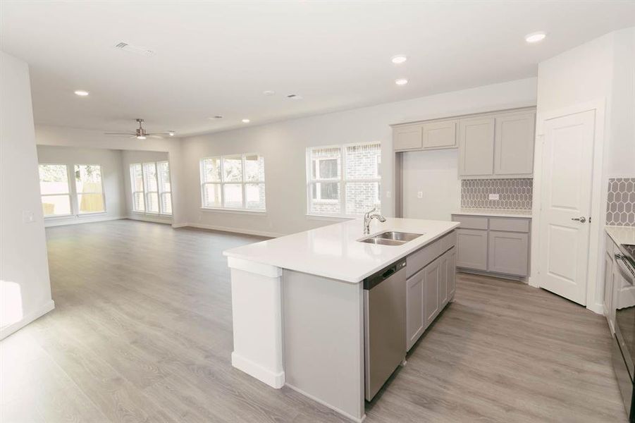 Kitchen with an island with sink, light wood-type flooring, decorative backsplash, stainless steel dishwasher, and sink