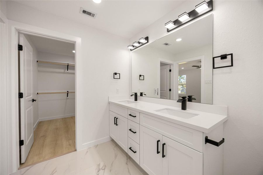 Primary bath showcasing a double vanity with ample storage, contemporary lighting, and convenient access to the walk-in closet for added functionality. Primary bath showcasing a double vanity with ample storage, contemporary lighting, and convenient access to the walk-in closet for added functionality.
