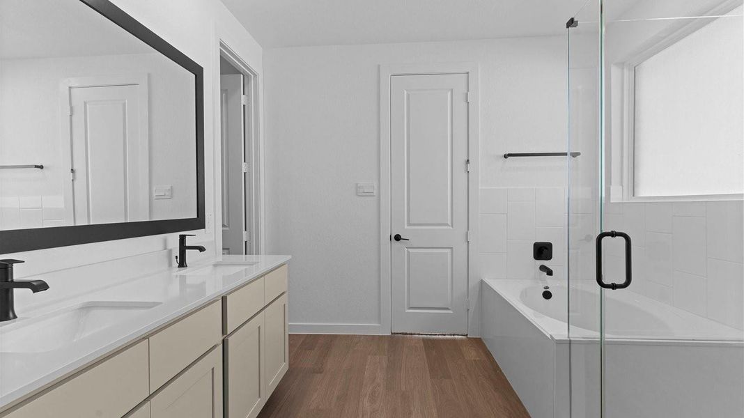 Luxurious primary bathroom with dual vanities, a soaking tub, glass-enclosed shower and walk-in closet.